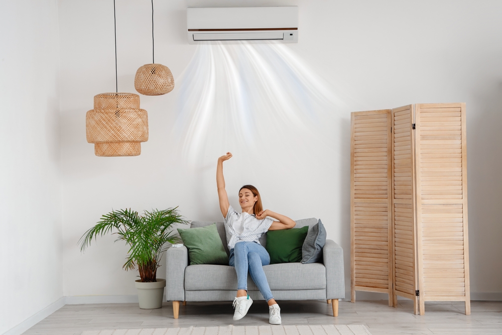 Young,Woman,With,Working,Air,Conditioner,Sitting,On,Sofa,At